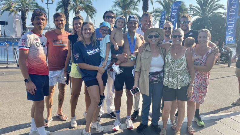 Agrandir l'image Un groupe d'hommes et de femmes posent tout sourire autour du MDC Guillaume qui porte un enfant dans les bras. En arrière plan des palmiers qui se détachent sur un grand ciel bleu.