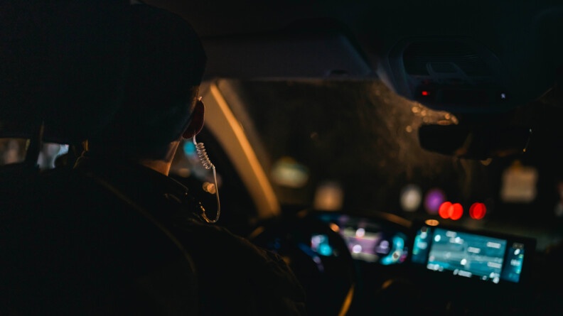 Un gendarme de dos dans une voiture. Il fait nuit et sombre.