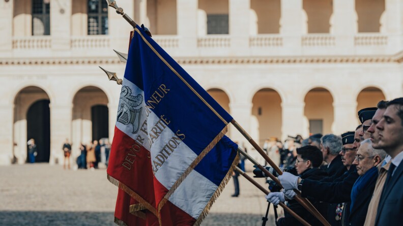 Des drapeaux saluent, tenus par des gendarmes, dans la cour ensoleillée des invalides