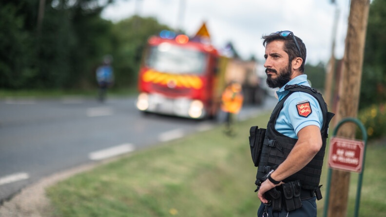 Un gendarme de profil gauche le long de la route, en arrière plan un camion de pompiers