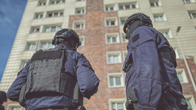 Deux gendarmes en tenue d'intervention devant une barre d'immeuble.