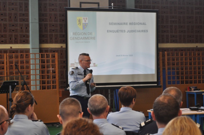 Photo d'un gendarme, de face, debout, tenant un micro dans sa main droite,s'exprimantn face &agrave; une assembl&eacute;e. La sc&egrave;ne s ed&eacute;roule dans une salle ferm&eacute;e.