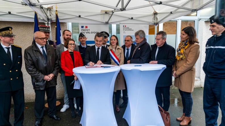 Le ministre de l'Intérieur, entouré d'autorités civiles et militaires, et de représentants d'associations de protection animale, debout derrière deux tables hautes recouvertes de toile blanche, en train de signer un document.