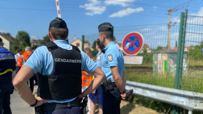 Au premier plan, un gendarme vu de dos et un autre de profil ; au second plan, un policier &agrave; gauche et des agents SNCF, &agrave; proximit&eacute; d'un passage &agrave; niveau.
