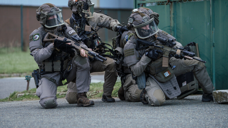 Trois militaires du GIGN, casqu&eacute;s, cagoul&eacute;s, visi&egrave;res baiss&eacute;es, fusils en joue, sont post&eacute;s, accroupis, &agrave; c&ocirc;t&eacute; d'un conteneur vert.