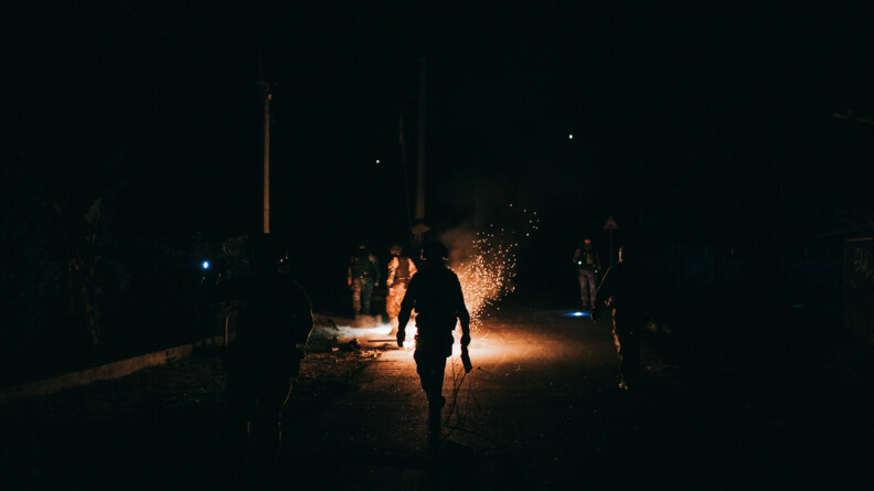 Agrandir l'image De nuit, dans une rue où brûle quelqeu chose sur la route, des gendarmes sont présents en tenue de maintien de l'ordre