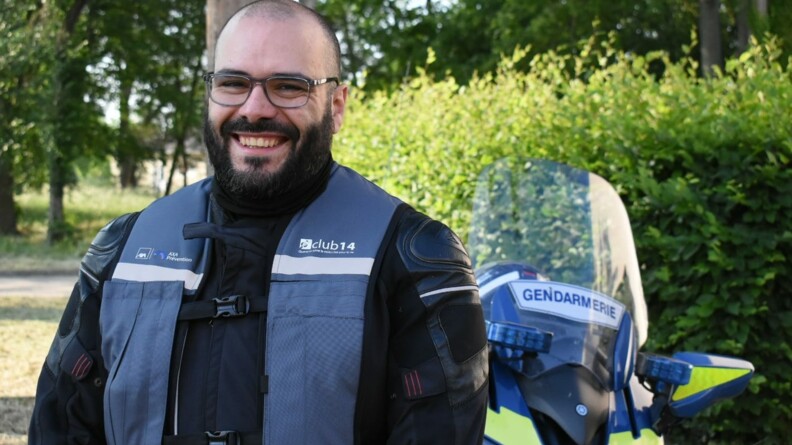 Un motard civil vu de face, arborant un grand sourire, ainsi qu'un gilet airbag offert par AXA pr&eacute;vention. En arri&egrave;re-plan, une moto de l'EDSR 78.