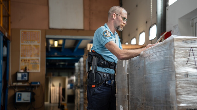 Un gendarme doté d'un exosquelette lombaire regarde des notes au-dessus de carton sous emballages et empilés