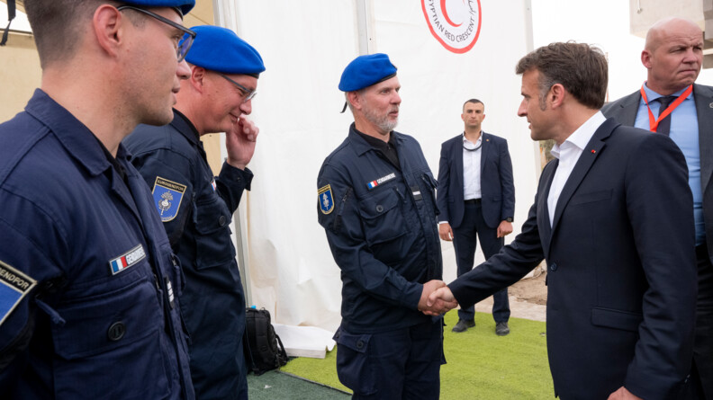 Agrandir l'image Le président de la République serre la main à un gendarme portant un béret bleu. Deux autres gendarmes portant la même tenue se tiennent sur la gauche. Deux personnes en civil sont en arrière plan.