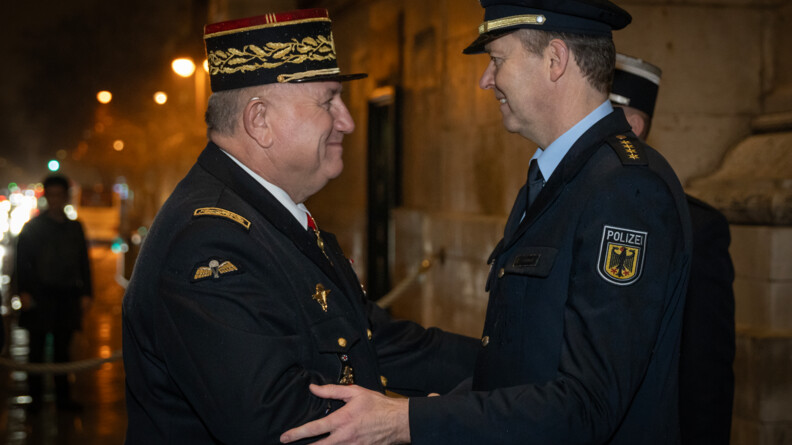 Un g&eacute;n&eacute;ral de gendarmerie francais et un policer allemand se serre la main avec chaleur, de nuit, en ville, sous la pluie