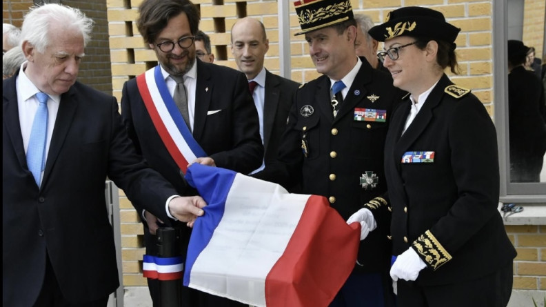 Une préfète, un général de gendarmerie, un élu porteur d'une écharpe tricolore et un homme en costard tiennent un drapeau français