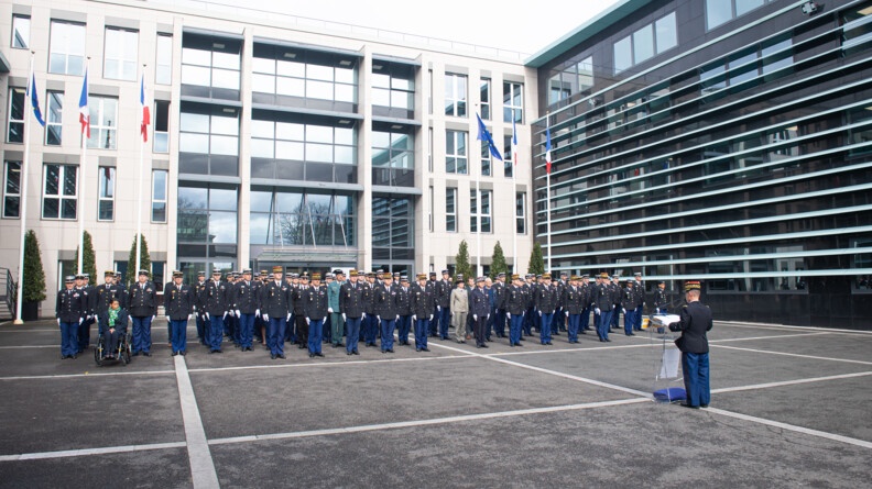 Une centaine de personnels de la direction générale de la gendarmerie en rang dans la cour d'honneur lors de la lecture de l'ordre du jour par le major général que l'on voit de dos.