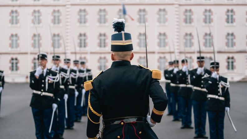 Agrandir l'image Des gendarmes en tenue de cérémonie sur 2 colonnes sur la place d'armes devant un bâtiment, au présentez sabre. Au milieu, de dos, un officier en tenue de tradition