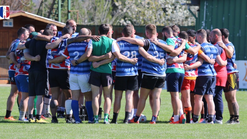 Environ 25 hommes en tenue de rugby, de diff&eacute;rentes couleurs, en cercle, se tiennent par les &eacute;paules et le dos