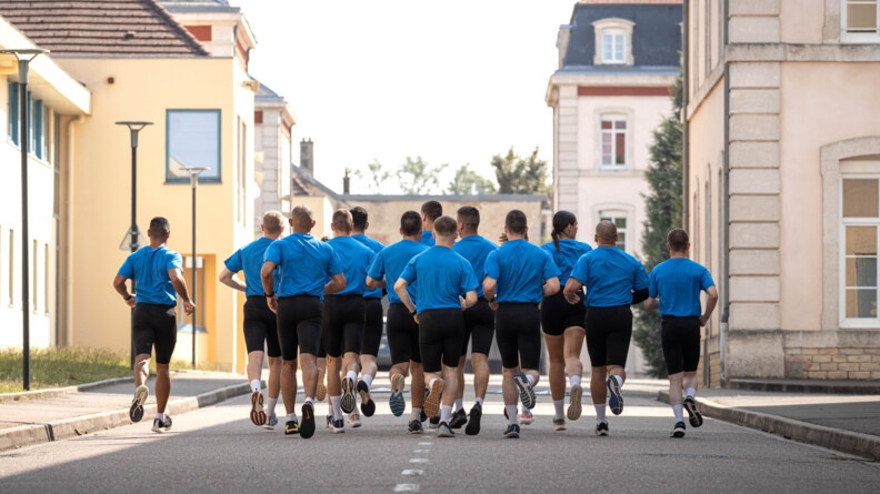 Vu de dos d'un groupe de sportifs en t-shirt bleu et cycliste noir dans une all&eacute;e entre des b&acirc;timents