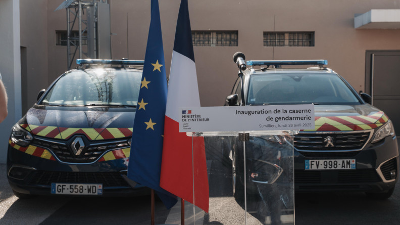 Agrandir l'image Deux véhicules de gendarmerie derrière un drapeau français et un drapeau européen, ainsi qu'un reposoir transparent portant la mention "inauguration de la caserne de gendarmerie"