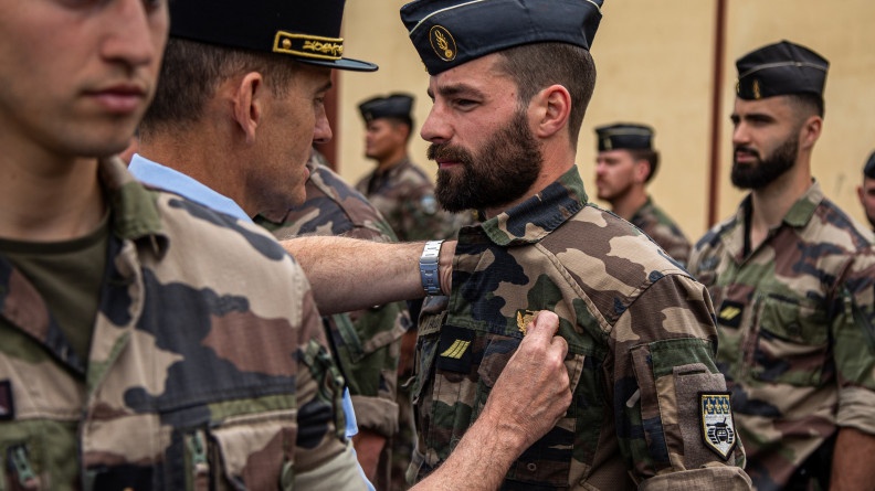 Un g&eacute;n&eacute;ral, de dos, &eacute;pingle un brevet sur la poitrine d'un militaire en treillis kaki.