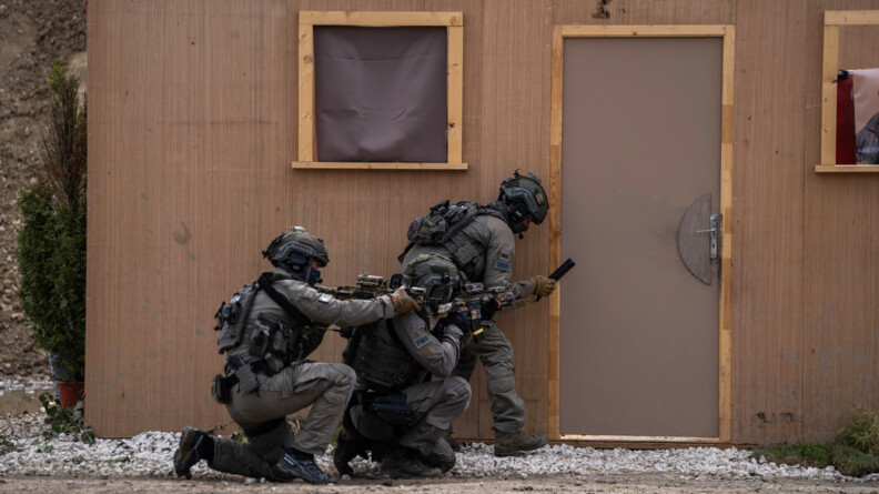 Trois militaires du GIGN en tenue kaki s'appr&ecirc;tent &agrave; mettre des explosifs au pied d'une porte d'un pr&eacute;fabriqu&eacute; en bois