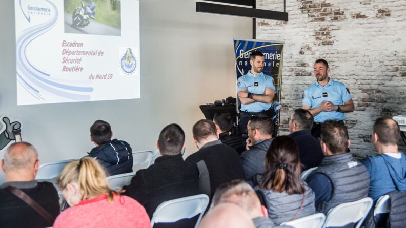 Devant un groupe assis sur des chaises, deux gendarmes présentent un power point projeté au mur sur la gauche