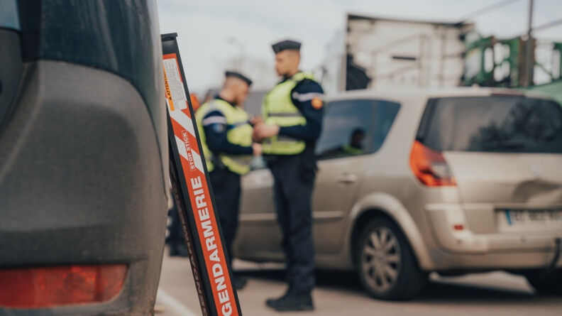 En premier plan un Stop-Stick et en fond et en flou, des gendarmes en train de controler un véhicule.