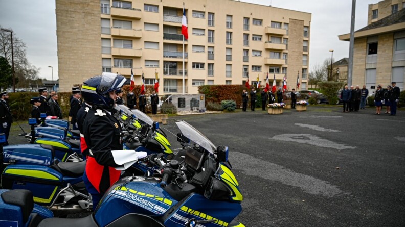 Au premier plan des motocyclistes de la gendarmerie de profil en grande tenue sur la place d'armes. En fond, de part et d'autre du mât des couleurs, une dizaine de porte-drapeaux.