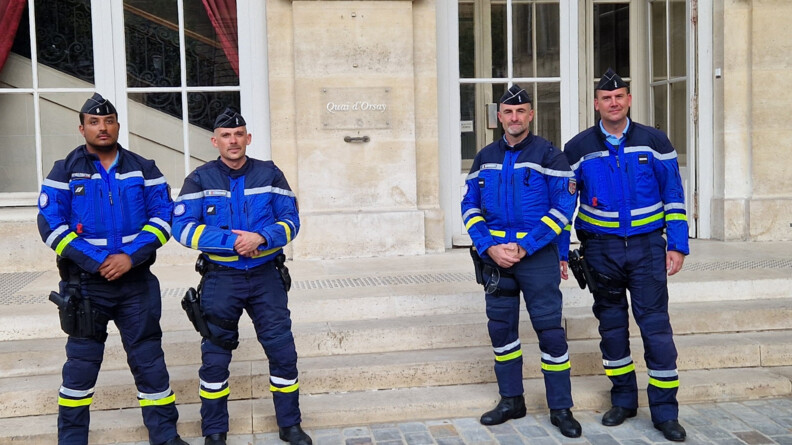 Quatre motards de la gendarmerie prennent la pause devant les marches du quai d'orsa; la façade du bâtiement est en pierres claires