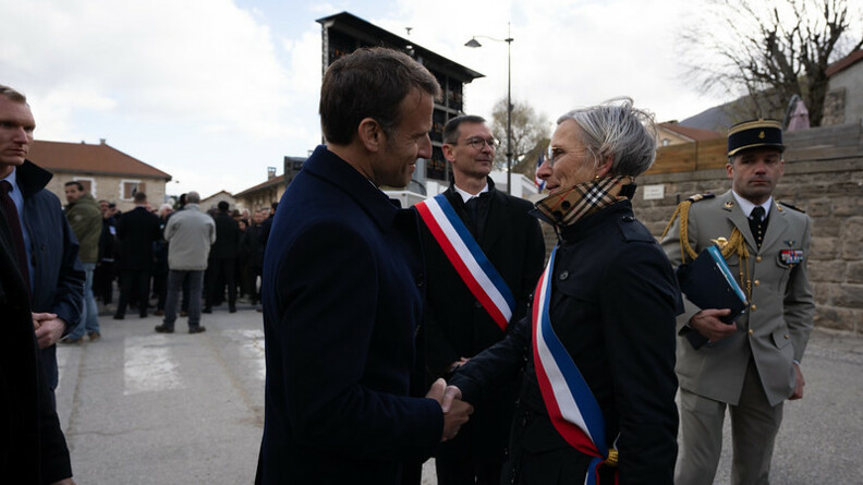 Agrandir l'image Le président de la République, Emmanuel Macron, vêtu d'un costume sombre, serre la main d'une femme vêtue d'un trench noir, et portant sur le torse l'écharpe tricolore.