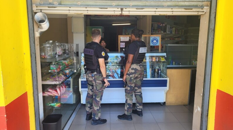 Deux gendarmes, que l'on aper&ccedil;oit de dos, debout, discutent avec une commer&ccedil;ante, apr&egrave;s le passage du cyclone Garance sur l'&icirc;le de la R&eacute;union.