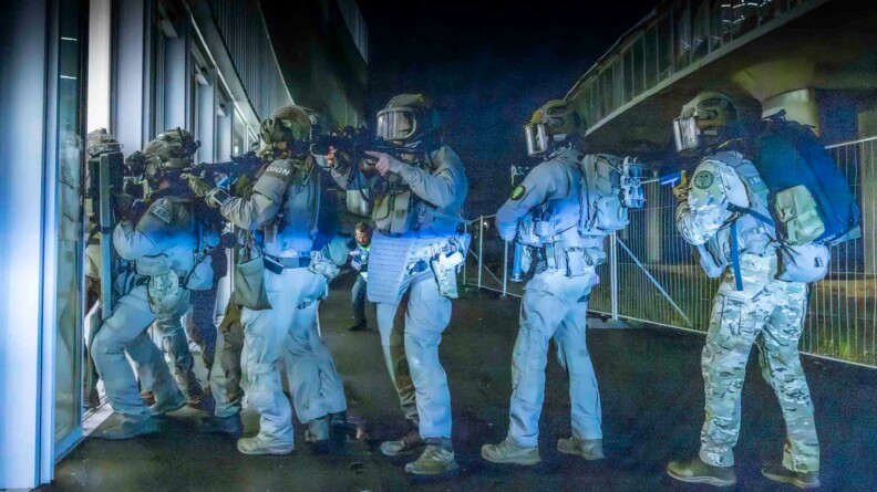Progression d'une colonne d'assaut de la force intervention du GIGN à l'extérieur du bâtiment Lumen, en train d'entrer par une porte vitrée.