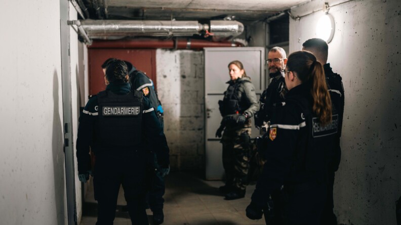 Dans le sous-sol d'un immeuble &eacute;clair&eacute; &agrave; la lumi&egrave;re artificielle, plusieurs gendarmes se tiennent debout c&ocirc;te &agrave;  c&ocirc;te. L'un d'eux inspecte un pan du mur.