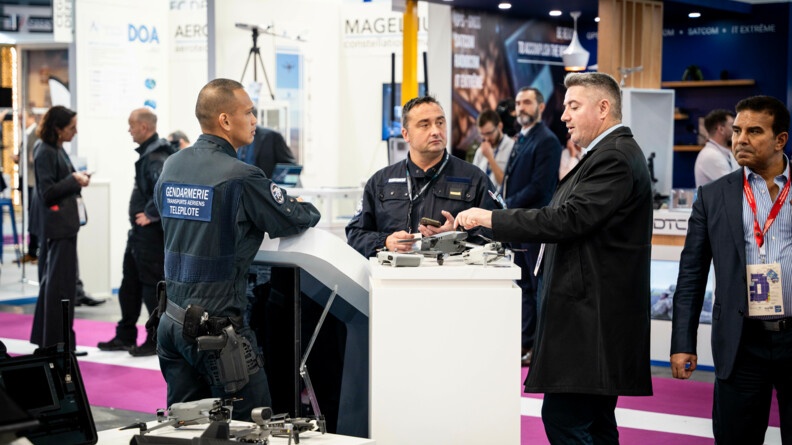Au stand de la gendarmerie sur Milipol, un gendarme t&eacute;l&eacute;pilote de dr&ocirc;ne, avec du mat&eacute;riel de lutte anti-drone, &eacute;change avec un autre gendarme et un homme en civil
