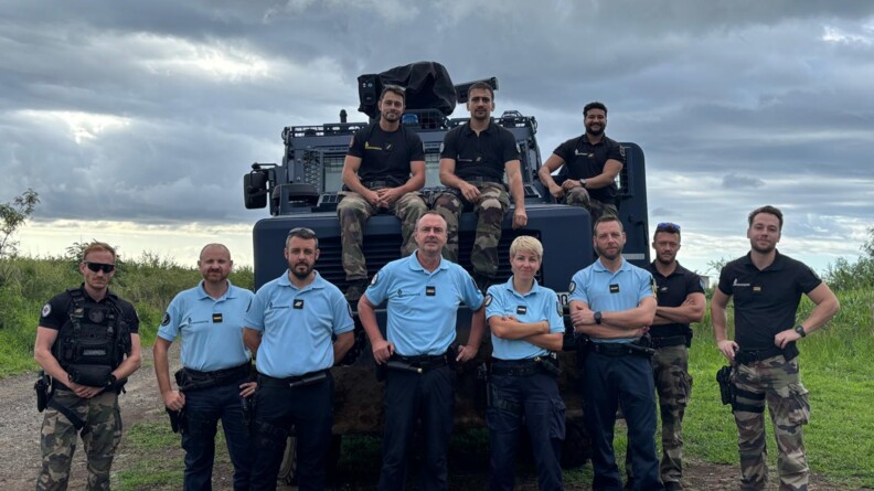 Agrandir l'image Onze gendarmes - dont cinq en tenue bleue eet six en tenue noire et kakie - posent devan tun véhicule blindé de la gendarmerie, à La Réunion, après le passage du cyclone Garance.