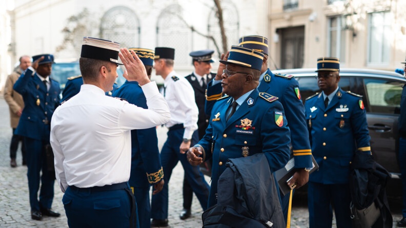 Agrandir l'image A l'extérieur, sur un sol pavé, se saluent des militaires de la gendarmerie congolaise et des militaires de la gendarmerie nationale, soit huit personnes au total. Tous portent le képi. En second plan, on aperçoit une voiture.