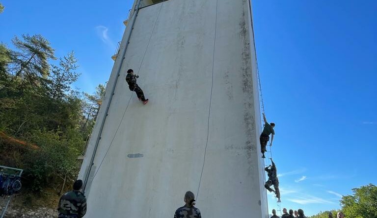 Agrandir l'image En extérieur, une dizaine de jeunes de la CPT attendent leur tour pour descendre en rappel le long de la paroi d'une grande tour.