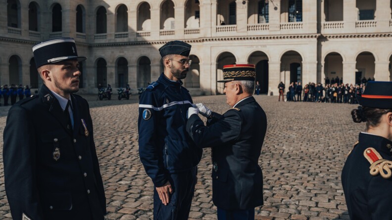 Un brigadier-chef de gendarmerie se voit remettre une m&eacute;daille par un g&eacute;n&eacute;ral d'arm&eacute;e de la gendarmerie dans la cour des Invalides