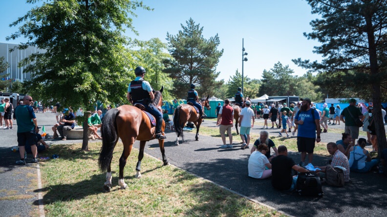 Trois cavaliers de la garde, vus de trois-quart dos, avancent l'un derri&egrave;re l'autre &agrave; travers la foule de supporters amass&eacute;e sur le parvis du stade.
