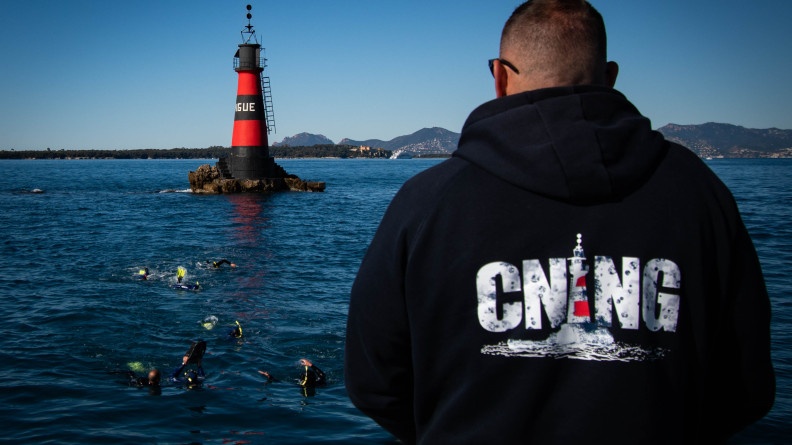 De dos, un instructeur du CNING regarde des plongeurs revenir d'un phare en mer.