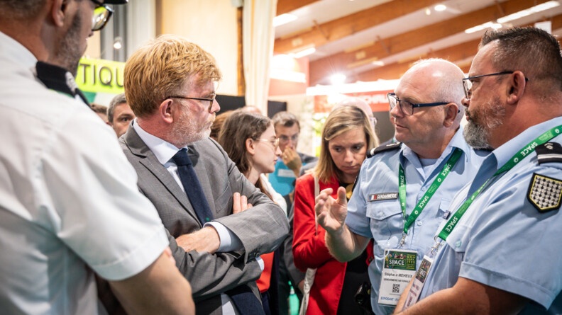 de profil regardant vers la droite, en complet gris et les bras croisés, le ministre de l'agriculture. Face à lui deux gendarmes. Derrière eux les visiteurs