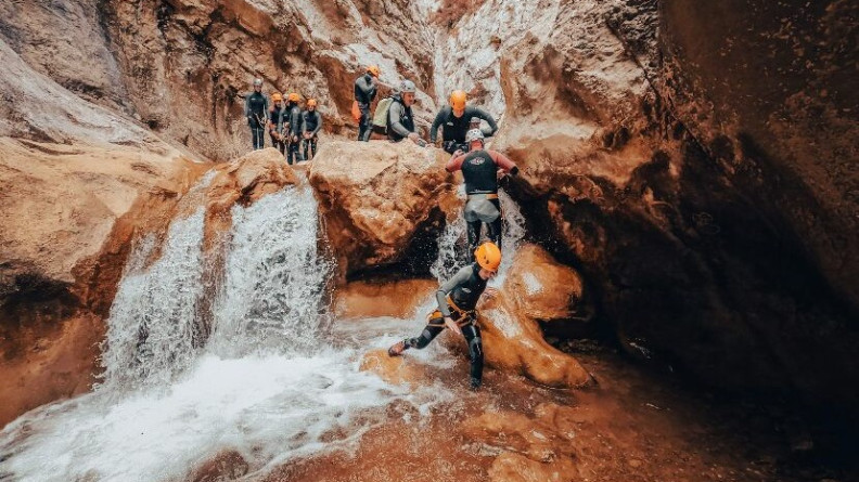 Neuf personnes en tenue de canyoning descendent une rivière au milieu d'une gorge rocheuse de couleur ocre.