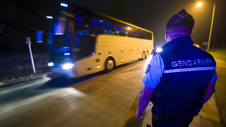 Gendarme de dos devant un bus circulant devant lui.