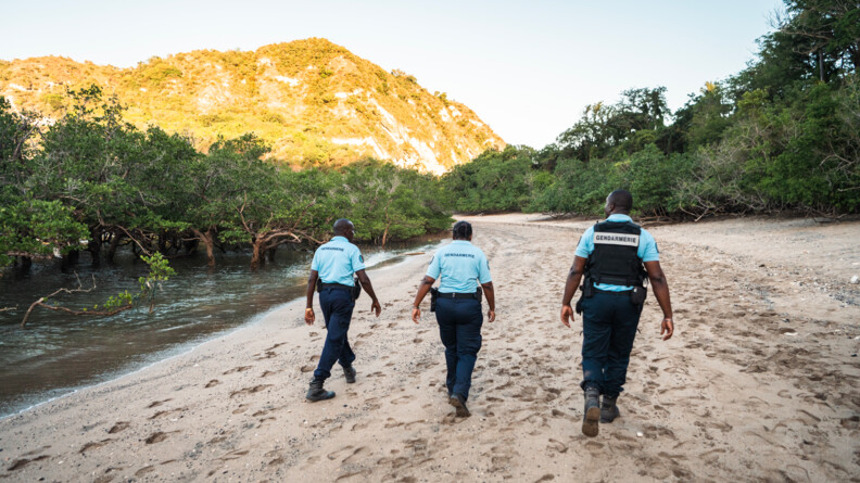 Trois réservistes de dos patrouillent sur la plage déserte.