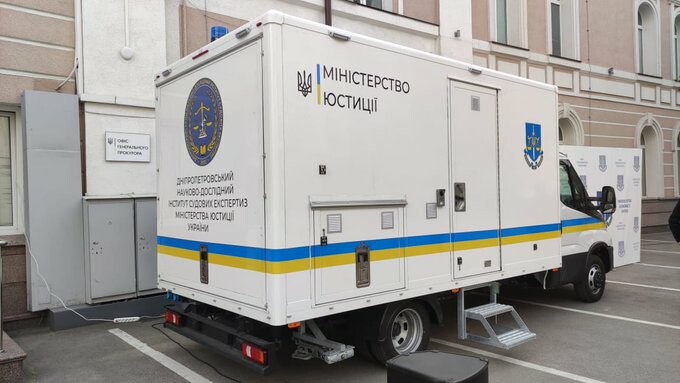 Agrandir l'image Un camion blanc avec un liseré aux couleurs du drapeau ukrainien et portant des inscriptions dans la langue du pays, garé sur le parking d'un bâtiment.