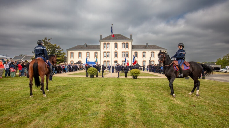 Deux cavaliers de la Garde républicaine avec en rrière plan une cérémonie de lever des couleurs.