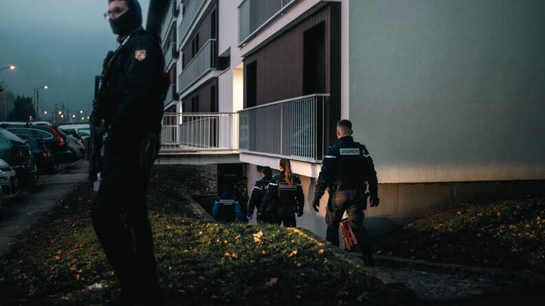 Des gendarmes s'approchent d'un immeuble, la nuit, dans lequel ils s'appr&ecirc;tent &agrave; p&eacute;n&eacute;trer, tandis qu'un autre militaire se tient en faction devant le b&acirc;timent, surveillant ainsi les abords.
