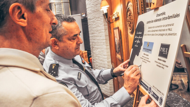 Le général de corps d'armée de la gendarmerie Olivier Courtet, commandant de la région des Hauts-de-France, signe une grande pancarte actant ainis la convention. A ses cotés, le directeur général de la société Holder, Maxime Holder, propriétaire des magasin Paul, tient la pancarte.