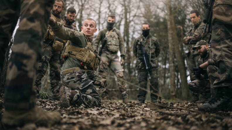 Une dizaine de gendarmes et militaires en treillis dans la forêt autour d'un qui explique la manoeuvre