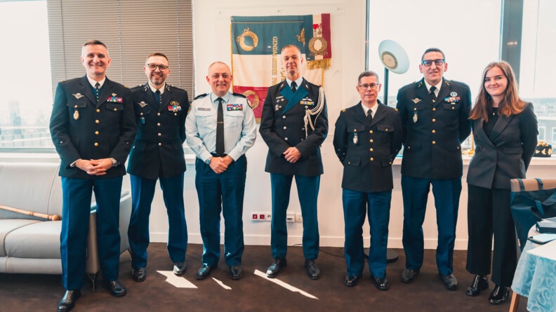 Six militaires, ainsi qu'une civile, se tiennent debout, c&ocirc;te &agrave; c&ocirc;te, dans une pi&egrave;ce. Tous regardent l'objectif en souriant.