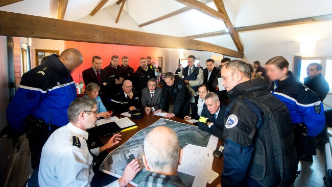 Agrandir l'image Au sein du poste de commandement opérationnel, les différentes autorités sont réunies autour d'une table où est posée une carte.