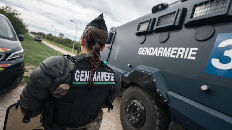 Agrandir l'image Une gendarme mobile de dos. A sa droite un véhicule blindé Centaure.