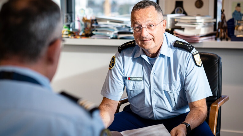Agrandir l'image Portrait du directeur général de la gendarmerie, assis sur un fauteuil, tenant un document entre les mains. Au premier plan, face à lui, un lieutenant-colonel vu de dos.